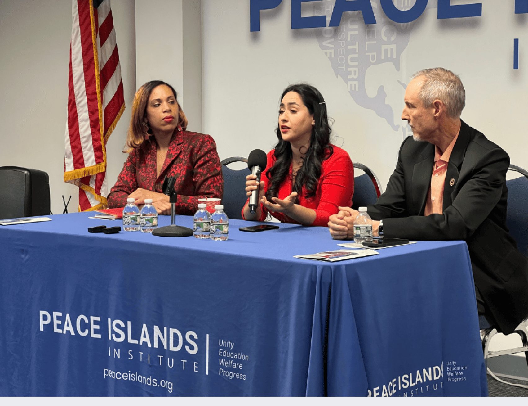 Three panelists speak at a table covered with a Peace Islands Institute tablecloth